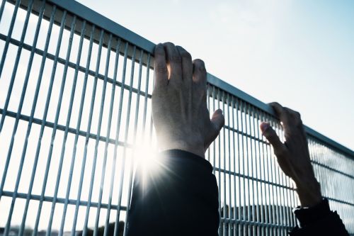 Man climbing up a metal fence — immigration consequences of criminal convictions concept.