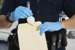 Midsection of a male police officer inserting drug packet in envelope during investigation